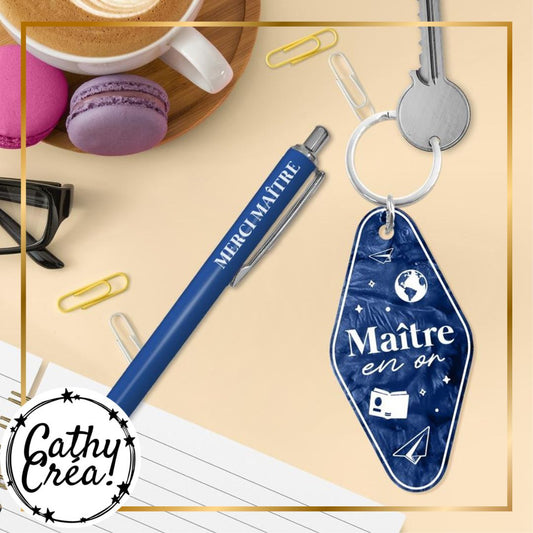 Stylo Merci Maitre et porte-cles Maitre en or poses sur bureau avec carnet et macarons