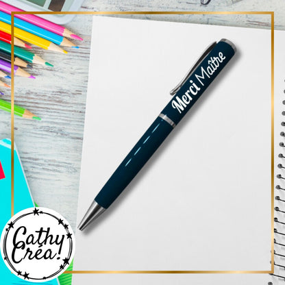 Stylo bleu marine inscription Merci Maitre en blanc pose sur carnet avec crayons de couleur