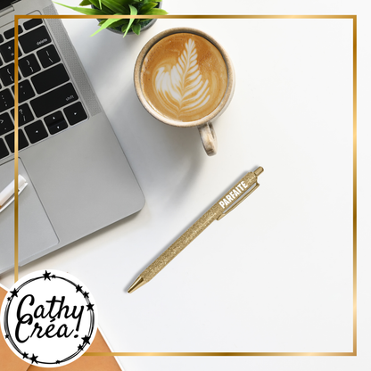 Stylo à paillettes dorées Parfaite posé sur un bureau avec laptop et café